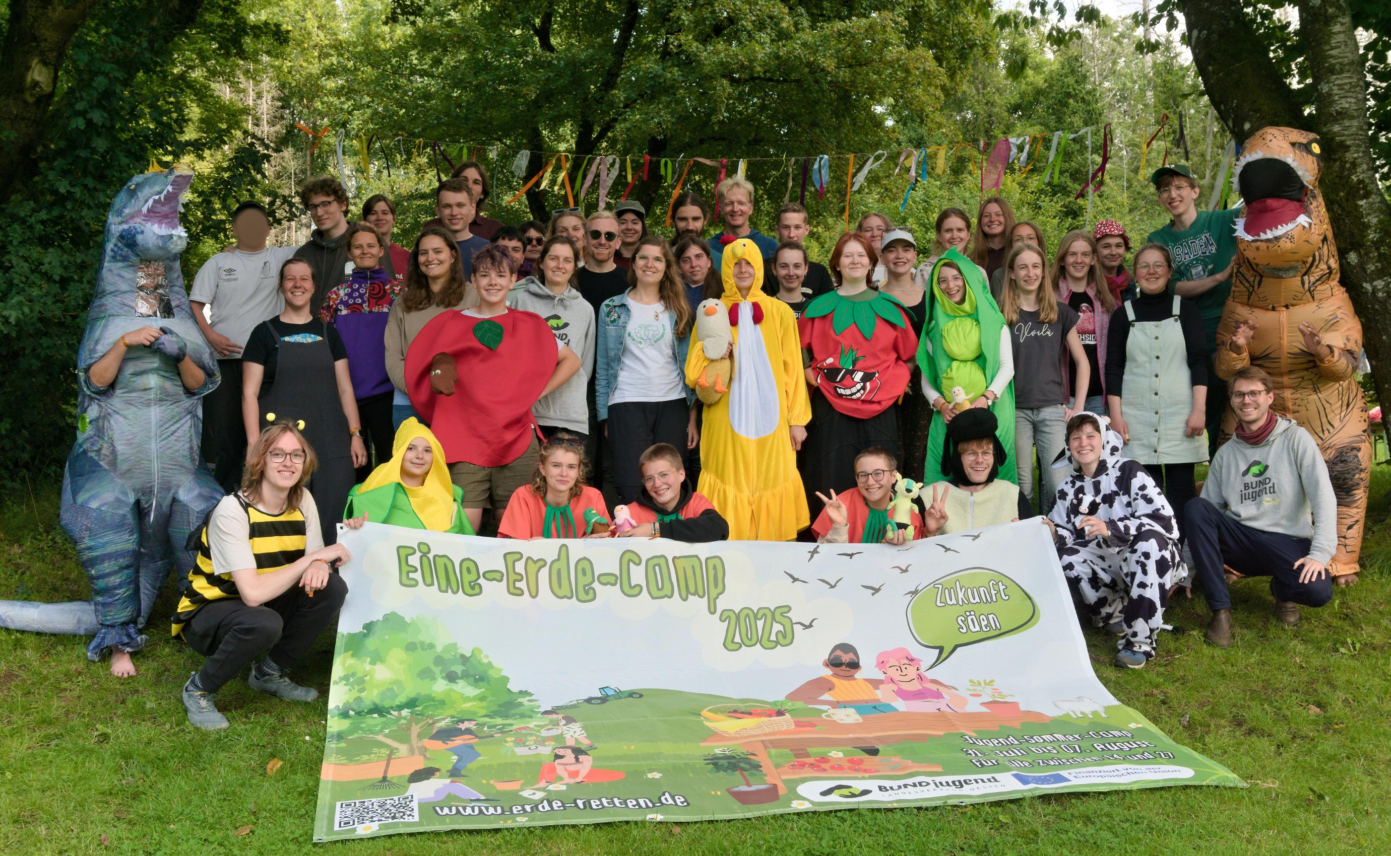 Eine Gruppe steht verkleidet hinter einem Banner wo Eine-Erde-Camp 2025 geschrieben steht