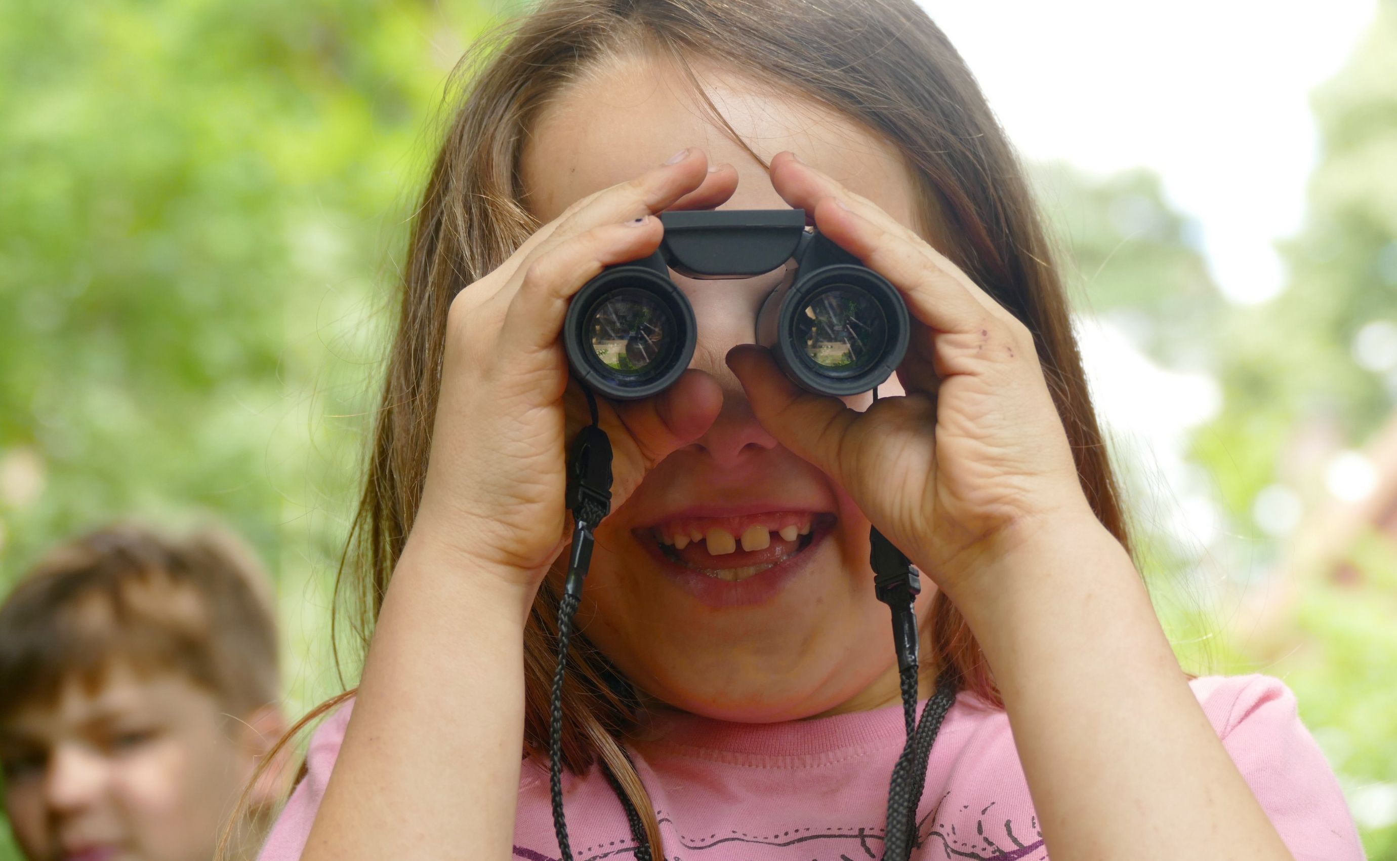 Kind schaut durch Fernglas im Freien.