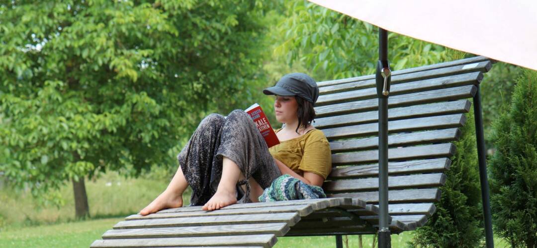 Person liest auf Holzbank im Garten und liest ein Buch.