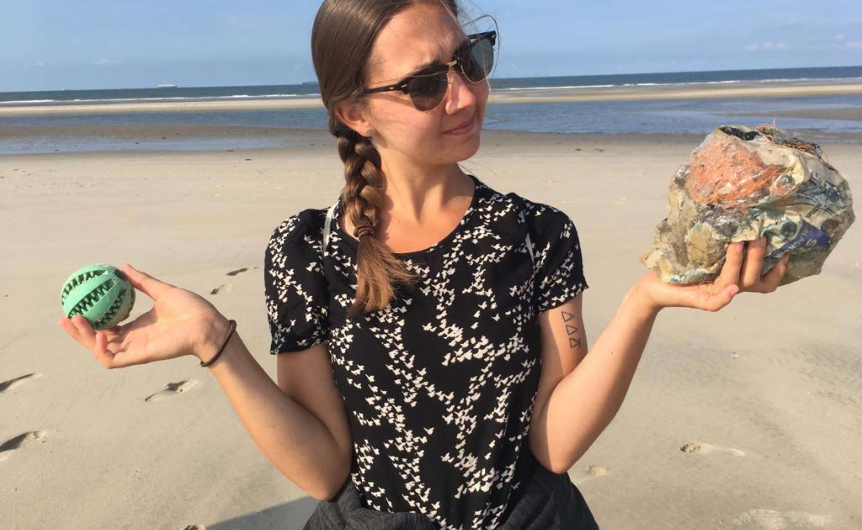 Frau am Strand mit Müll in beiden Händen.