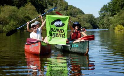 Menschen paddeln im Kanu auf Fluss, BUND Jugend Banner.