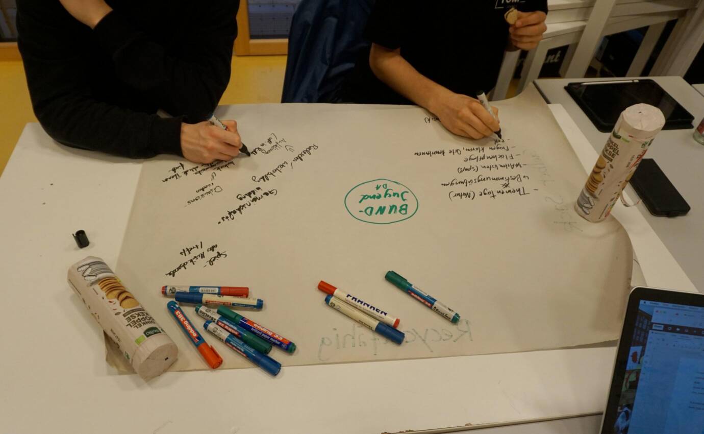 Menschen schreiben mit Stiften auf ein großes Papier.