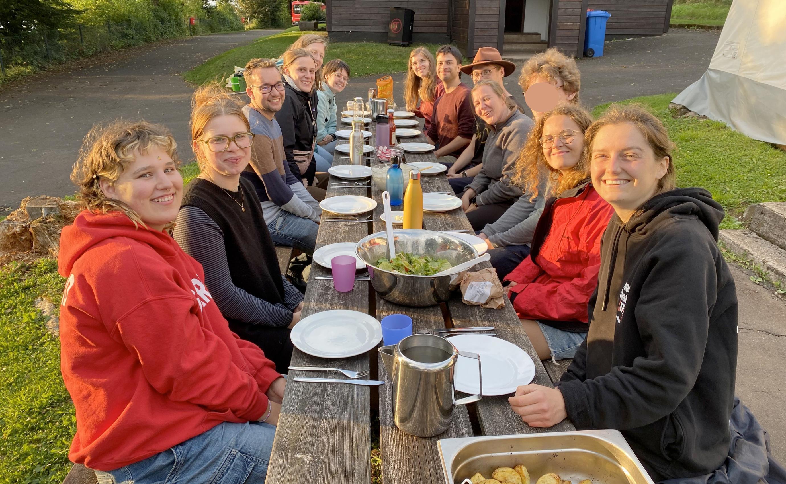 Gruppe isst gemeinsam an einem langen Tisch im Freien.