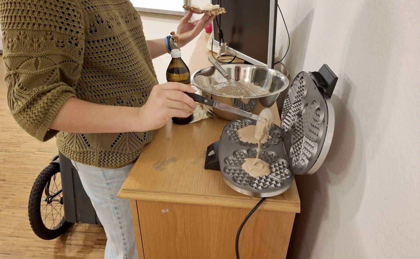 Eine Person trägt Teig auf ein Waffeleisen auf.