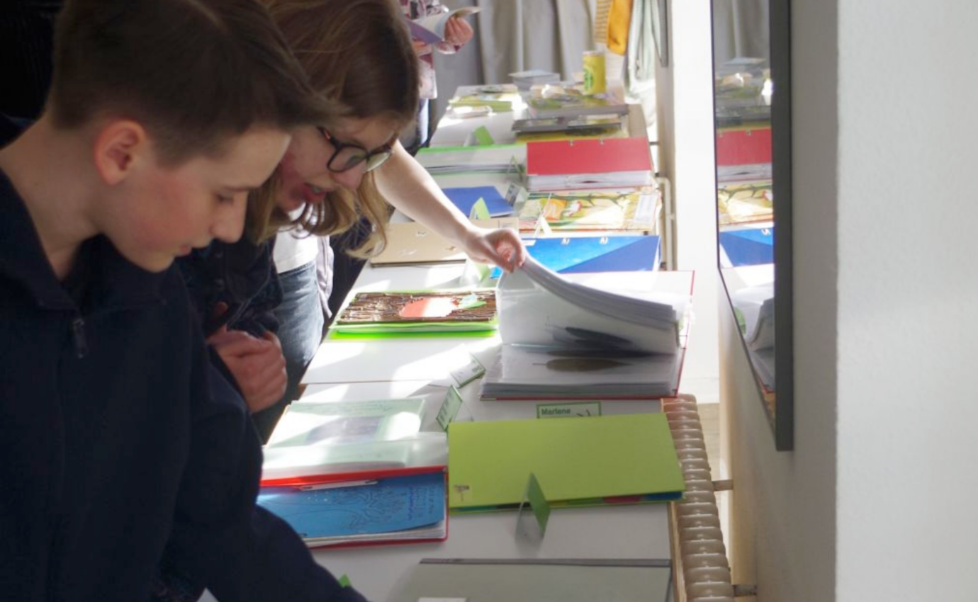 Schüler betrachten Arbeiten auf einem Tisch.
